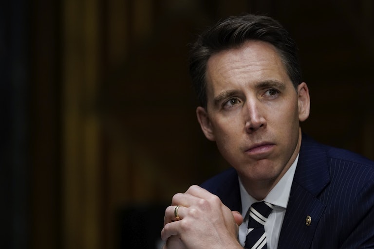 A close-up of Josh Hawley looking to the left with his hands clasped at his chest.