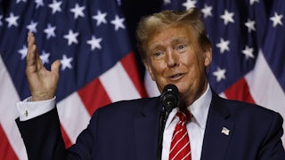 Donald Trump speaks at a mic and makes a very weird face. A U.S. flag is behind him.