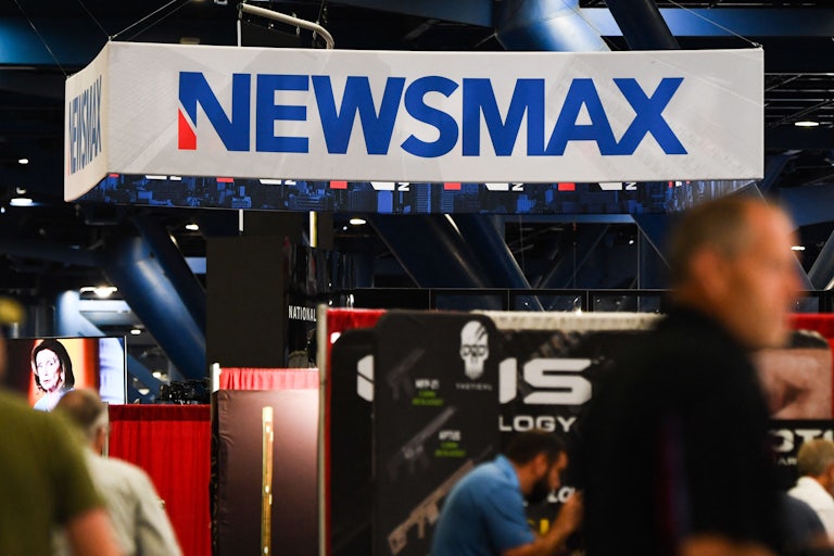 A giant white sign that reads "Newsmax." Others walk in front, out of focus.