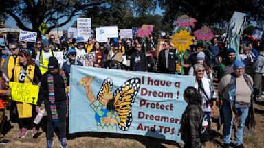 A group of protesters hold up banners against the Trump administration's immigration policies, with one banner reading "I have a dream! Protect Dreamers and TPS!"