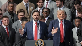 JD Vance speaks at a podium with Donald Trump beside him, flanked by other people.