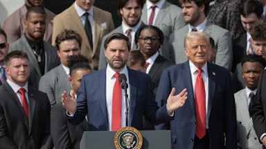JD Vance speaks at a podium with Donald Trump beside him, flanked by other people.