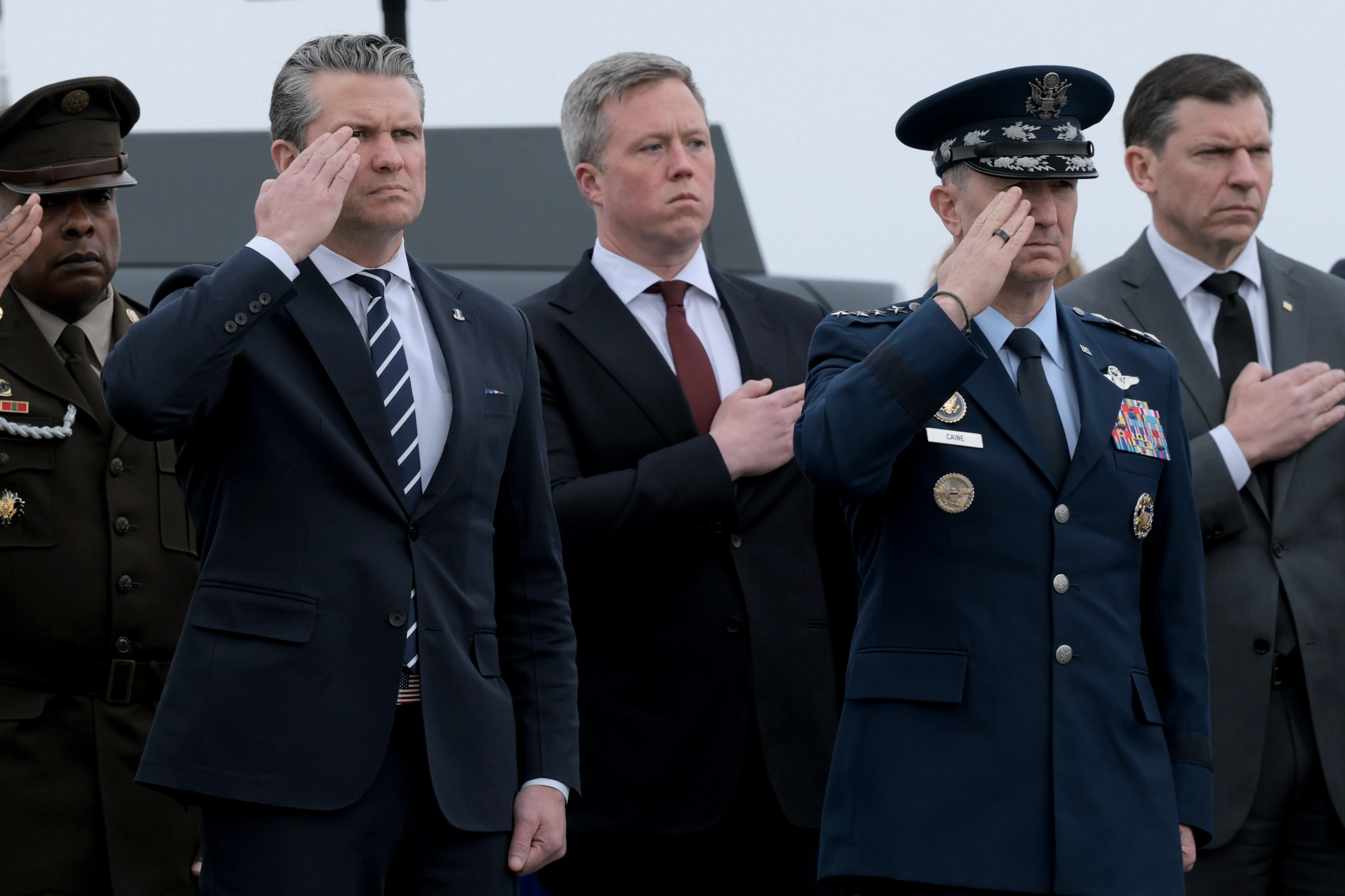 Defense Secretary Pete Hegseth and Army Secretary Daniel Driscoll stand at attention alongside three other men.