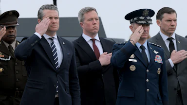 Defense Secretary Pete Hegseth and Army Secretary Daniel Driscoll stand at attention alongside three other men.