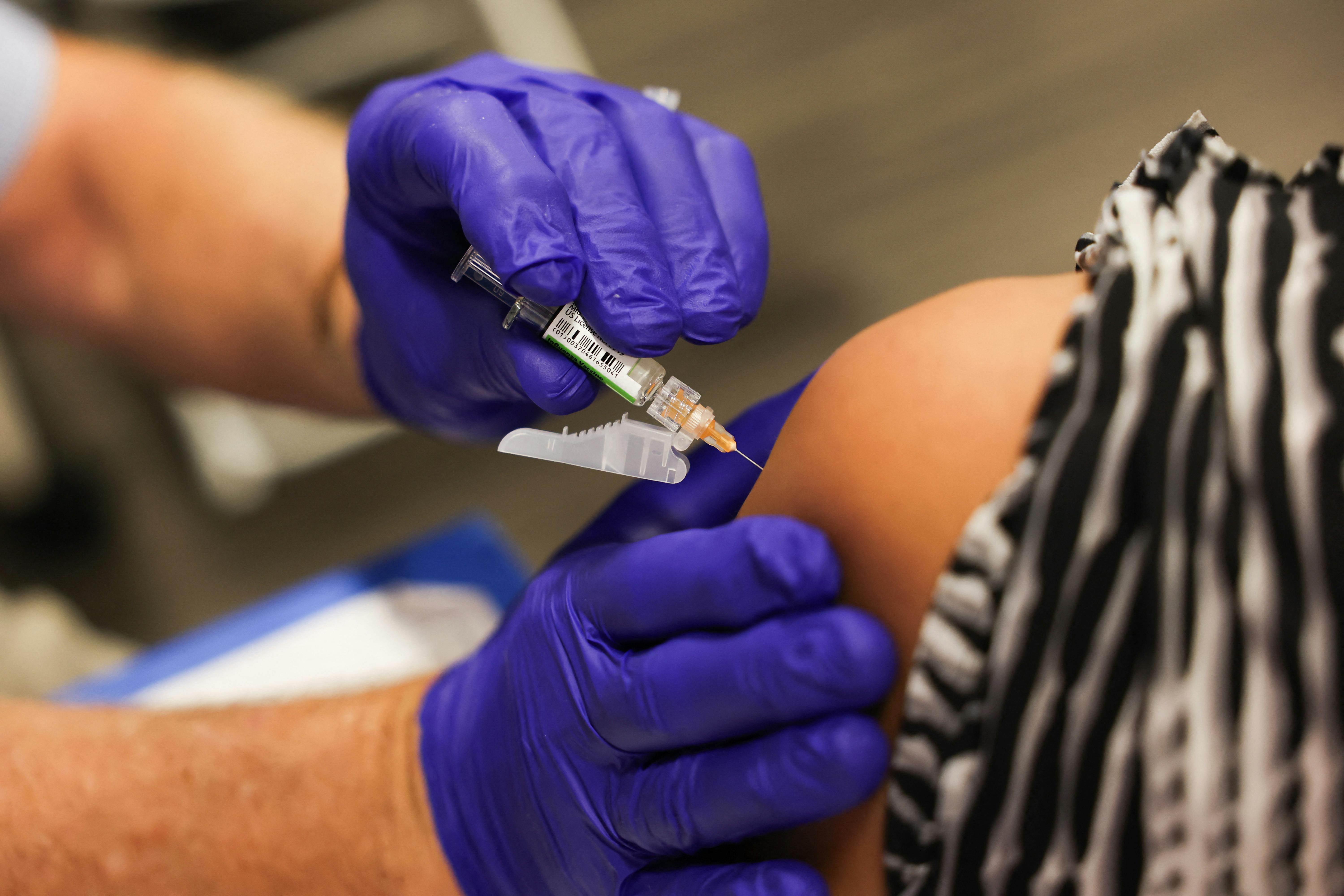 A person with purple gloves administers a vaccine dose in a syringe into another person's arm.
