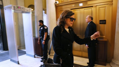 Representative Nancy Mace wears sunglasses while walking in the Capitol. She holds her left arm out in front of herself.