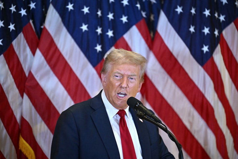 Donald Trump stands in front of American flags and speaks into a microphone