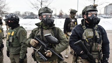 Three federal agents carrying guns and wearing gas masks.