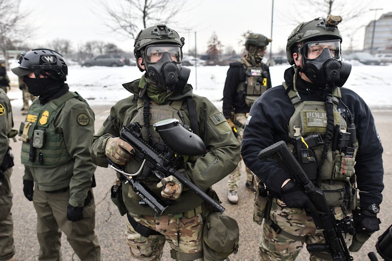 Three federal agents carrying guns and wearing gas masks.