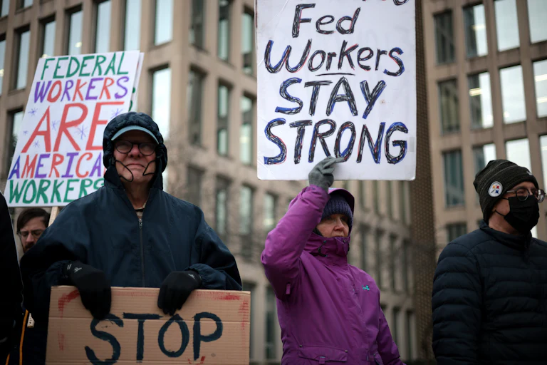 Protesters hold signs that read "Fed Workers Stay Strong" and "Federal Workers Are American Workers."