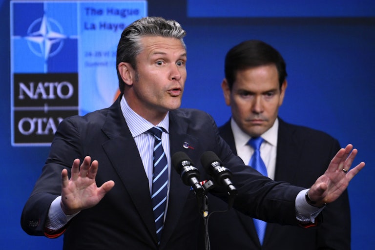 Defense Secretary Pete Hegseth gestures while speaking at a podium during the NATO summit at The Hague. State Secretary Marco Rubio stands behind him