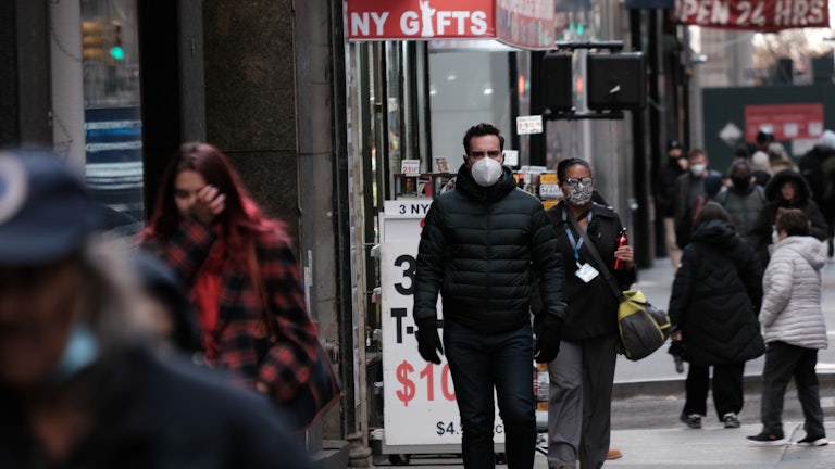 People walk on the sidewalk in Manhattan while wearing facemasks.