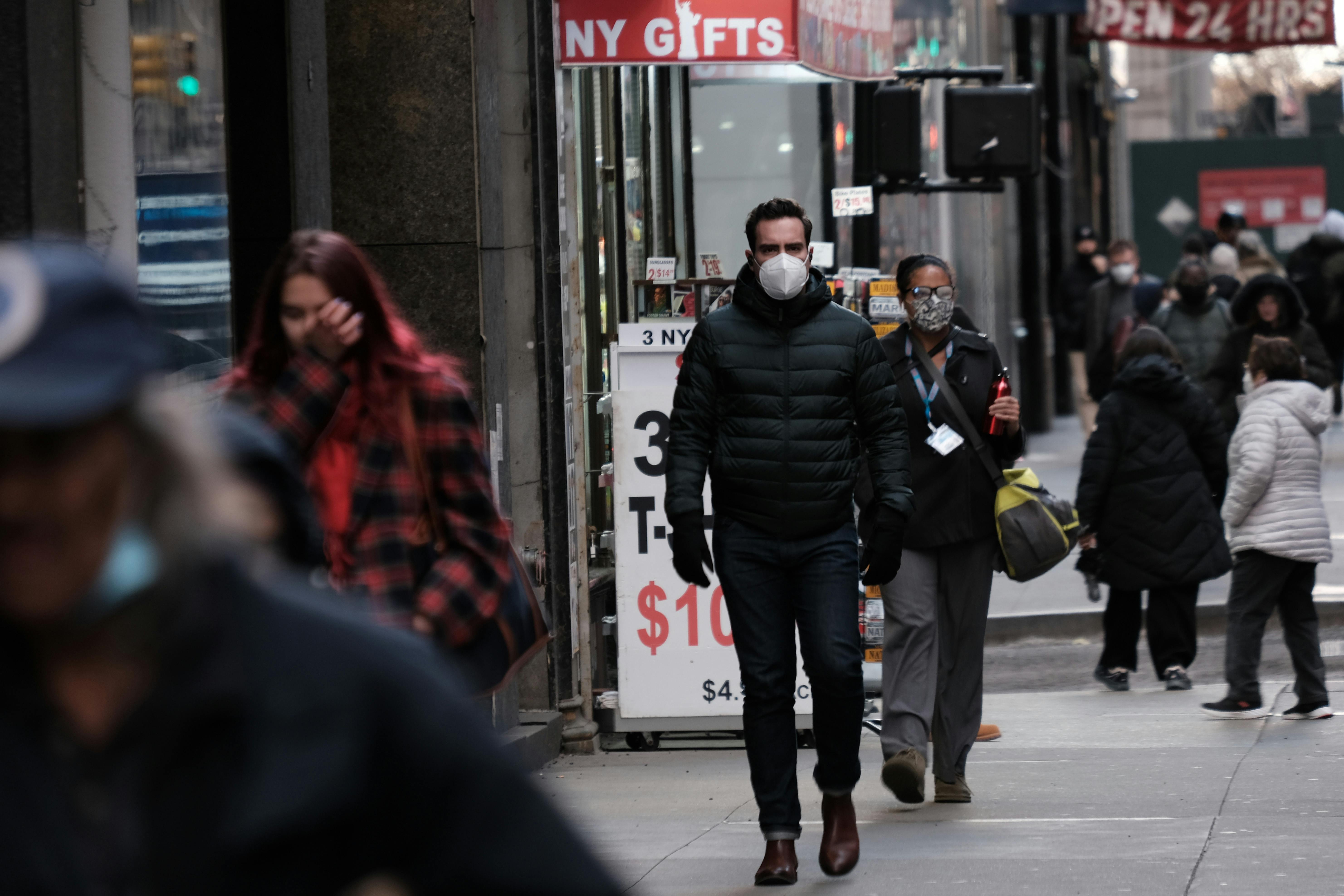 People walk on the sidewalk in Manhattan while wearing facemasks.