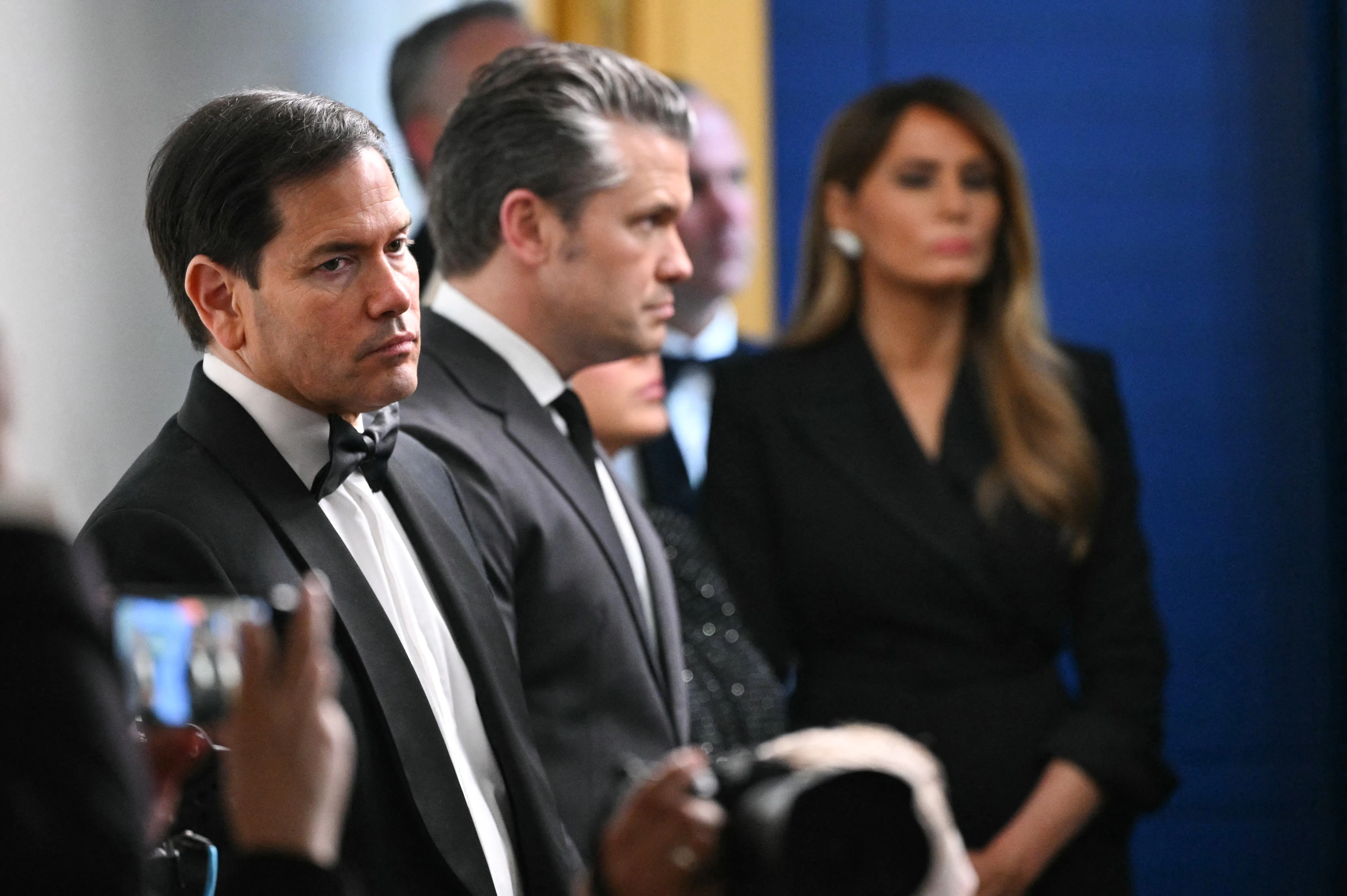 Secretary of State Marco Rubio and Defense Secretary Pete Hegseth dressed in black tie, with Melania Trump in the background. The photo was taken after the White House Correspondent's Dinner shooting.