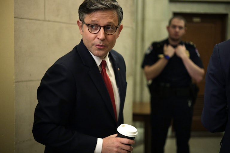 House Speaker Mike Johnson holds a coffee and looks over his shoulder.