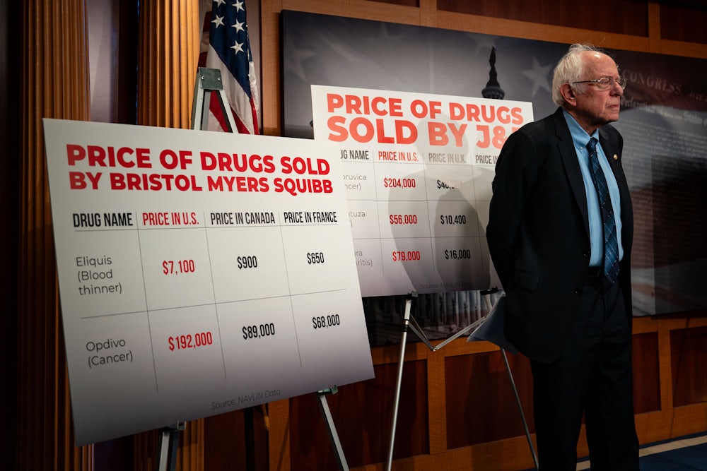 Vermont Senator Bernie Sanders stands in front of posters describing the extent to which pharmaceuticals cost more in the United States than in other countries.