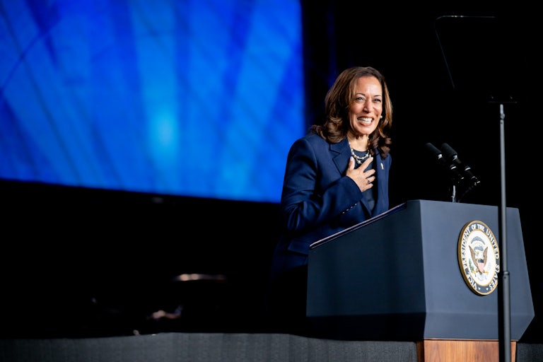 Kamala Harris holds her hand to her chest and smiles as she stands at a podium
