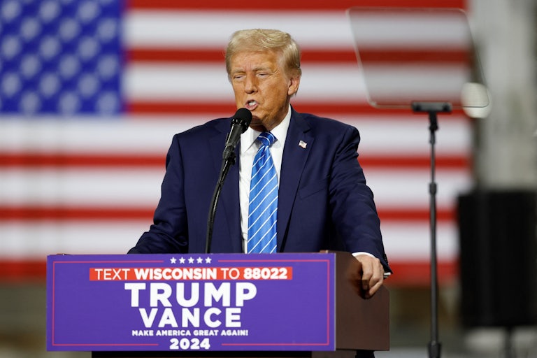 Donald Trump speaks into a microphone while standing next to a teleprompter