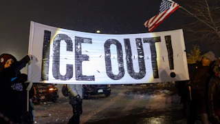 People hold up a banner that says, "ICE out!" during a protest in Minneapolis, Minnesota