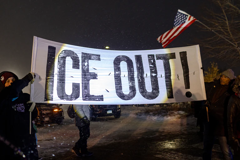 People hold up a banner that says, "ICE out!" during a protest in Minneapolis, Minnesota