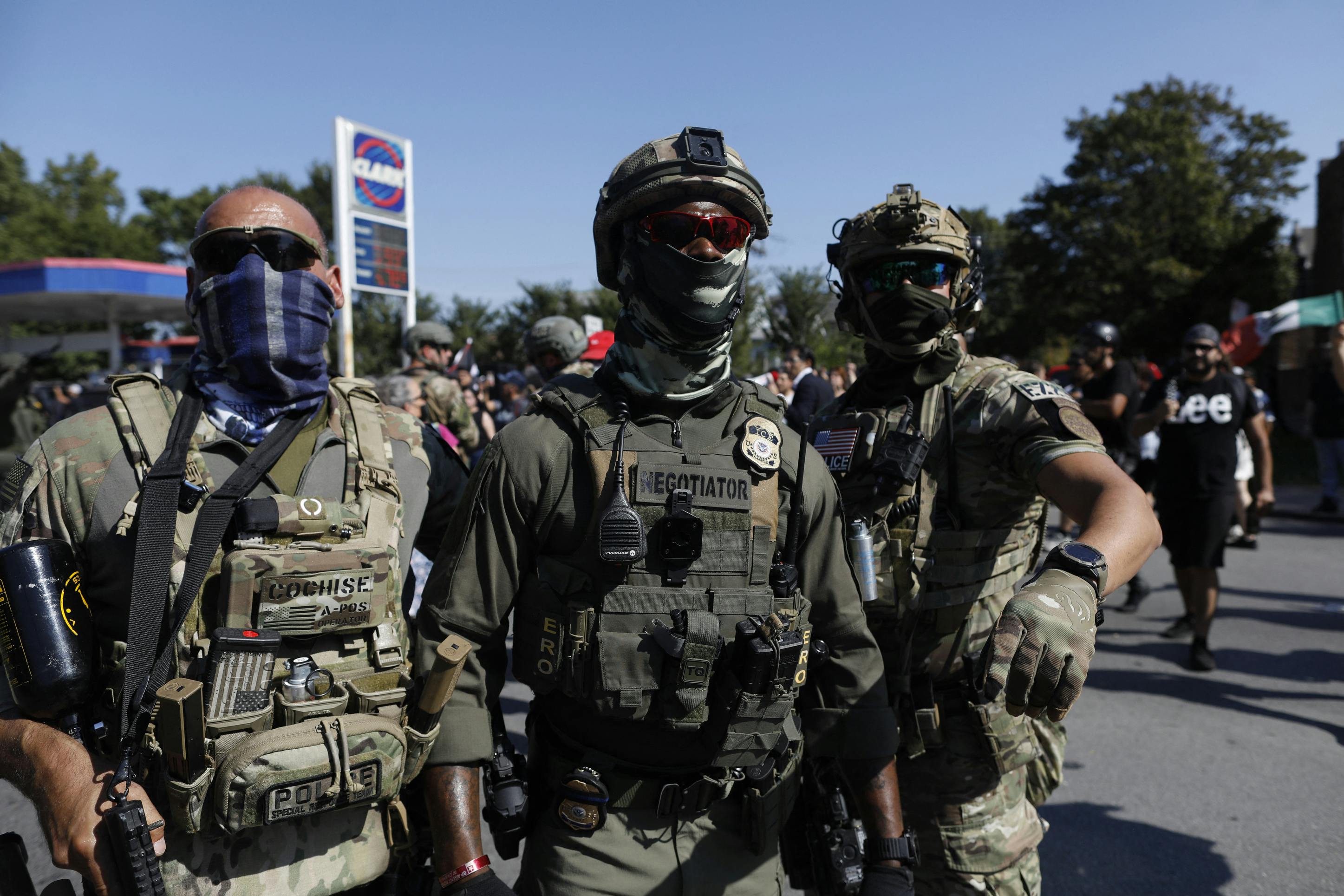 Three ICE officers stand in front of a gas station in Chicago