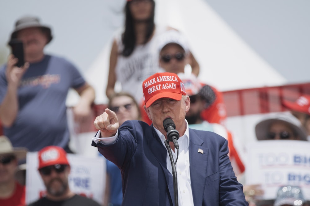 Donald Trump points toward the camera while speaking into a microphone.