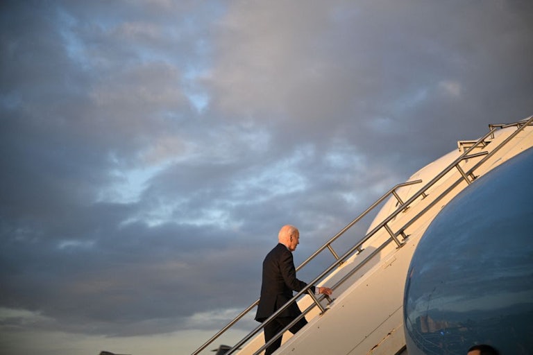 Biden climbs steps to Air Force One, with a clouded sky in the background.