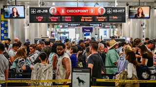 Screens play a video of Secretary of Homeland Security Kristi Noem as tons of travelers pass through Miami International Airport.