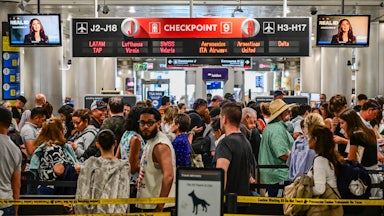 Screens play a video of Secretary of Homeland Security Kristi Noem as tons of travelers pass through Miami International Airport.