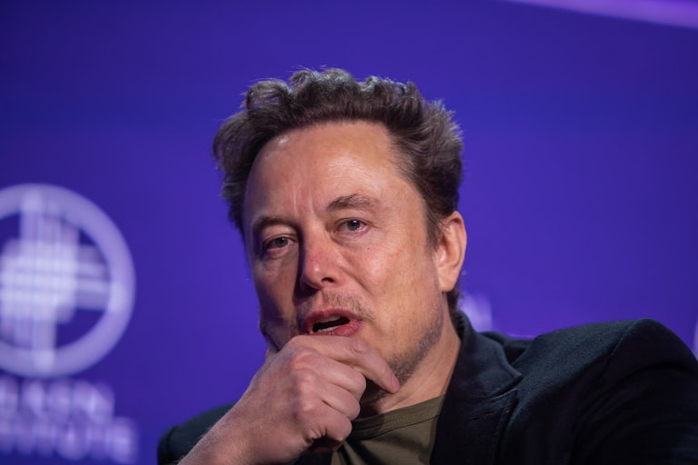 Elon Musk rests his chin on his hand as he speaks