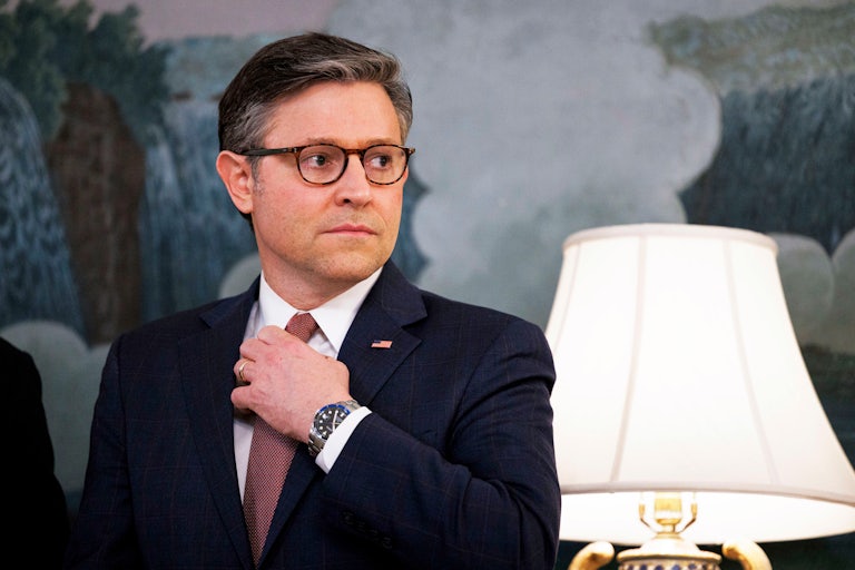 House Speaker Mike Johnson touches his tie while listening to a press conference by Donald Trump