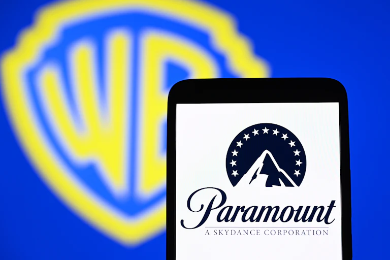 The Paramount Skydance Corporation logo is seen on a smartphone with the Warner Bros. logo in the background.