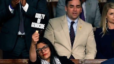 Rahida Tlaib wears a keffiyeh and holds up a sign that reads "Guilty of Genocide" while seated in the Capitol.