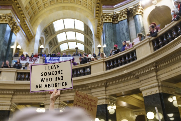 A bunch of people hold signs in the rotunda. In the forefront is a sign that reads "I love someone who had an abortion."