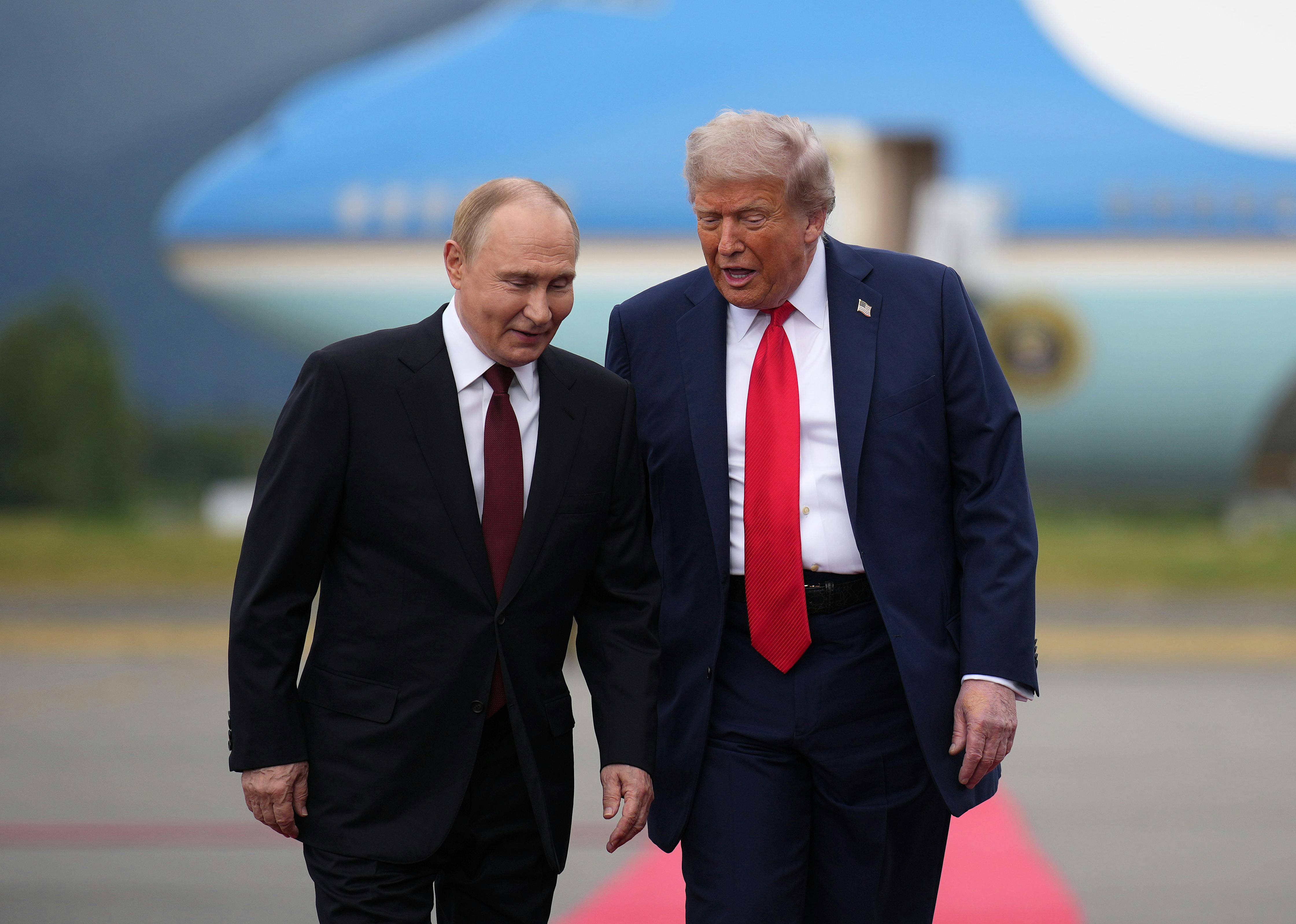 U.S. President Donald Trump walks with Russian President Vladimir Putin on a red carpet, as a plane is in the backgorund.