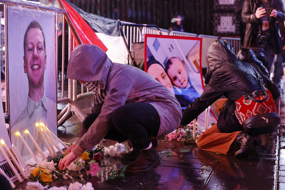 People in rain jackets light candles and crouch in front of pictures and flowers.