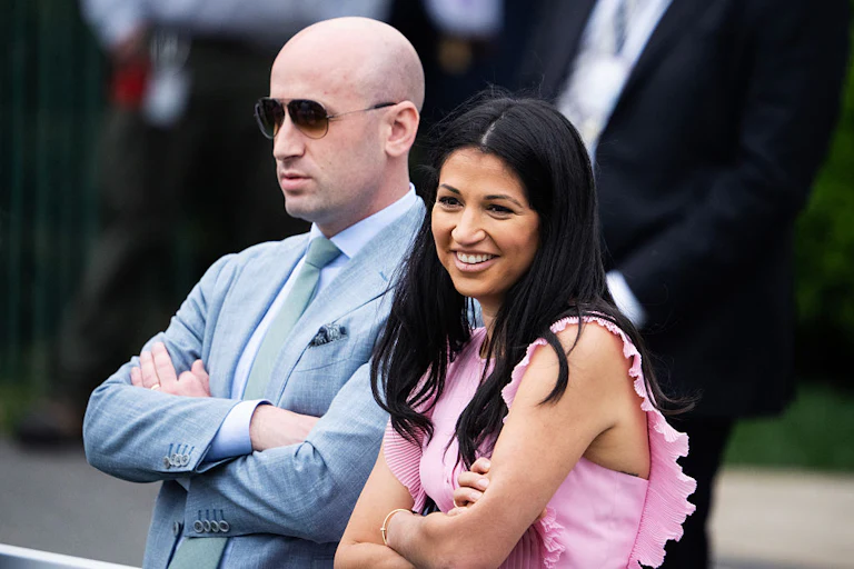 Stephen Miller stares into the distance as Katie Miller laughs. Both have their arms crossed.