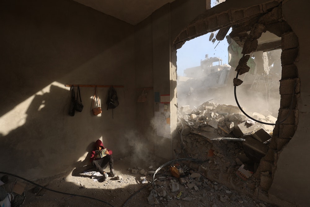 A photograph of a Palestinian boy holding a book as he sits in the rubble of a house at the Nuseirat refugee camp in the central Gaza Strip after overnight Israeli airstrikes in April 2025.
