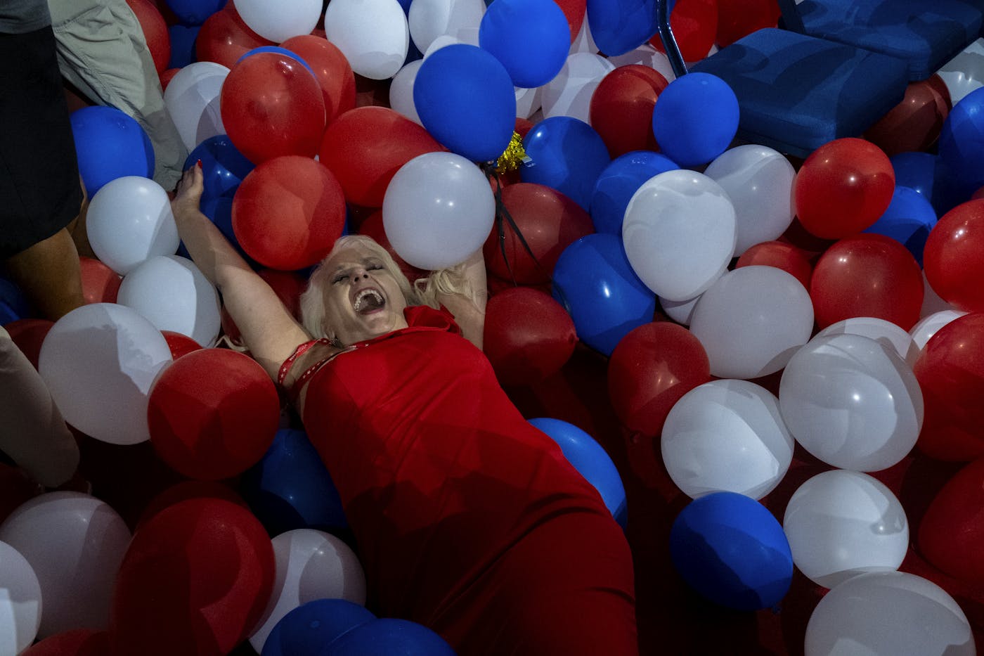 A photograph of a woman in a red dress joyfully laying in a pile of balloons the Republication National Convention 