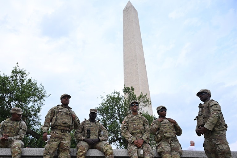 Members of the National Guard sit on a wall in front of the Washington Monument