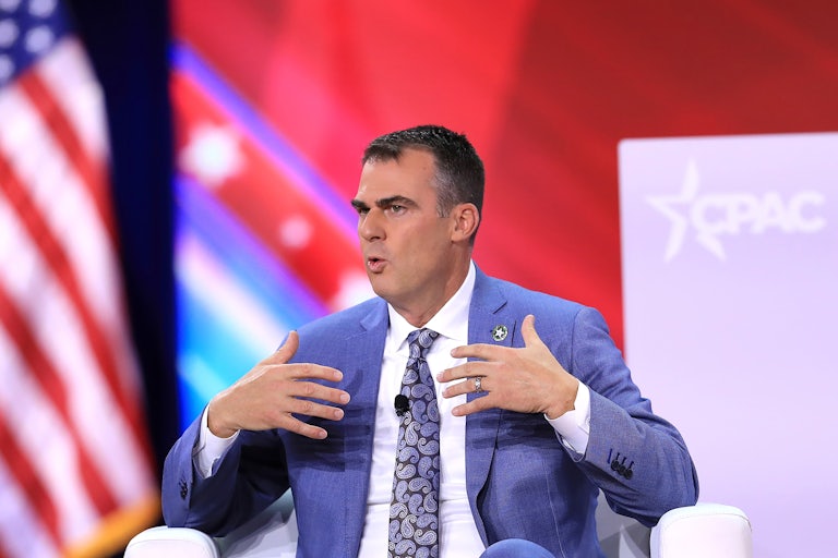 Kevin Stitt gesticulates while seated onstage.