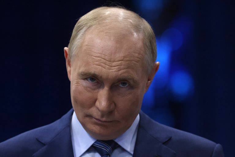 Vladimir Putin smiles and raises his eyebrows, chin tucked in, at the camera
