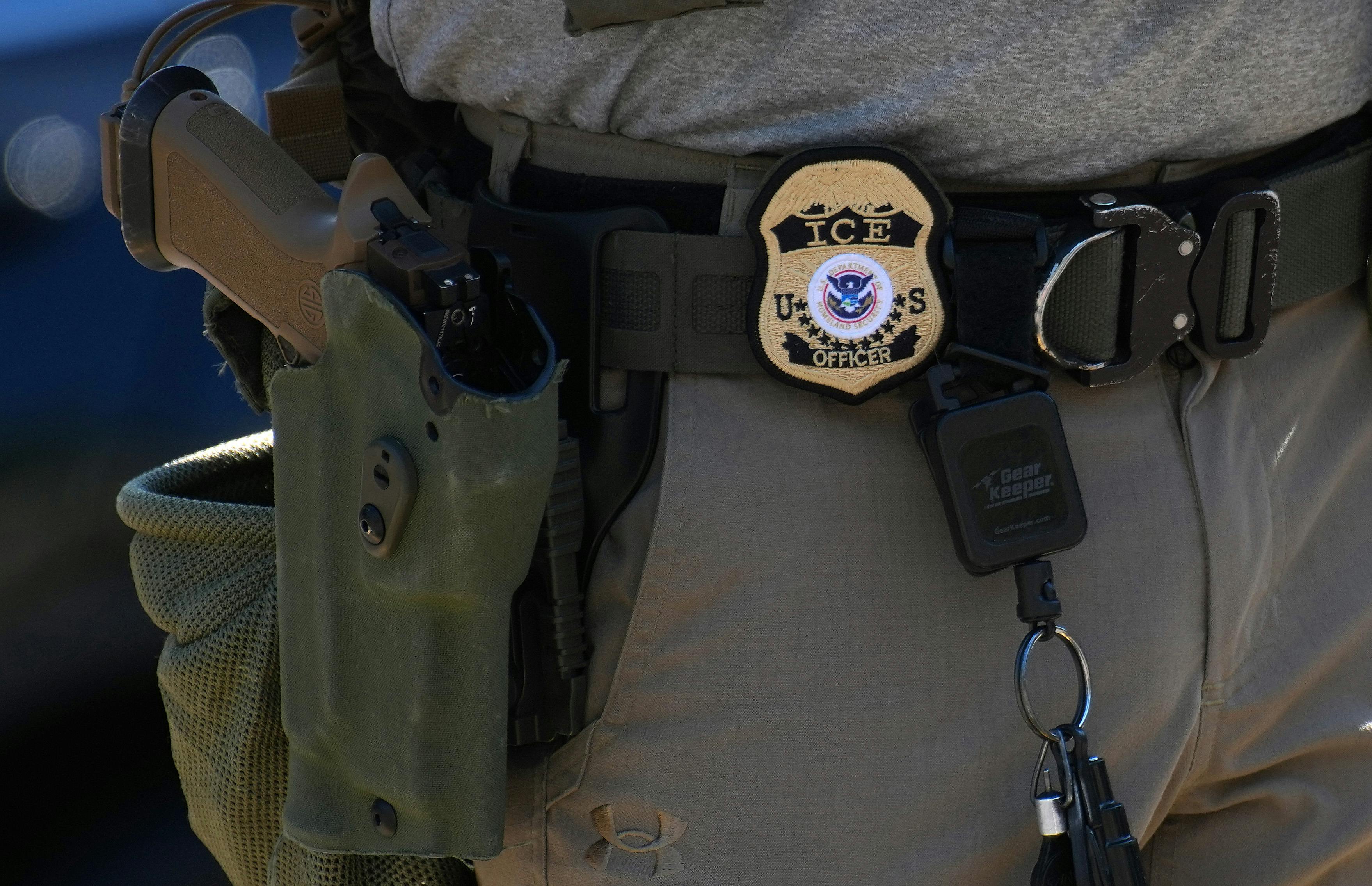 an ICE agent's badge and gun hanging off his belt
