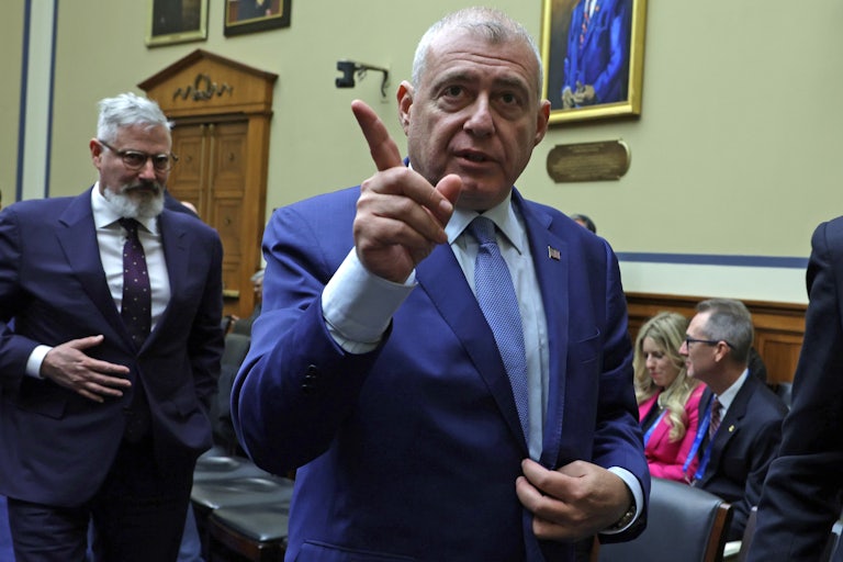 Lev Parnas walks in a Capitol room. One hand is on his suit jacket and he is pointing in the air to something off camera with the other.