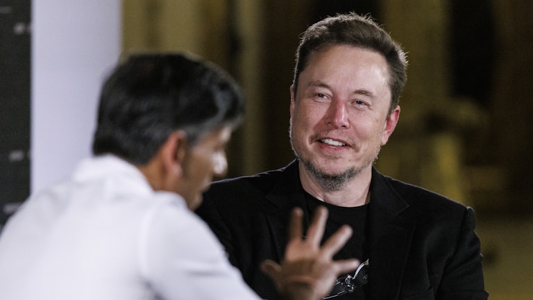 Elon Musk smiles at Rishi Sunak who gesticulates in the foreground.