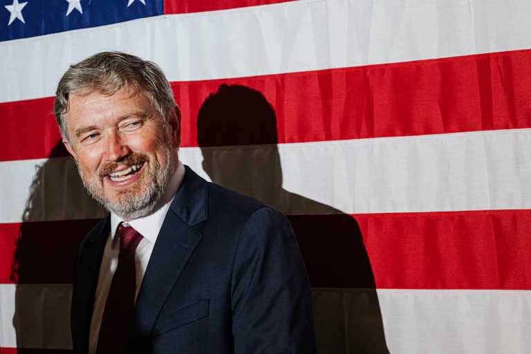 Representative Thomas Massie smiles and looks to the side after giving his primary concession speech. A large American flag hangs behind him