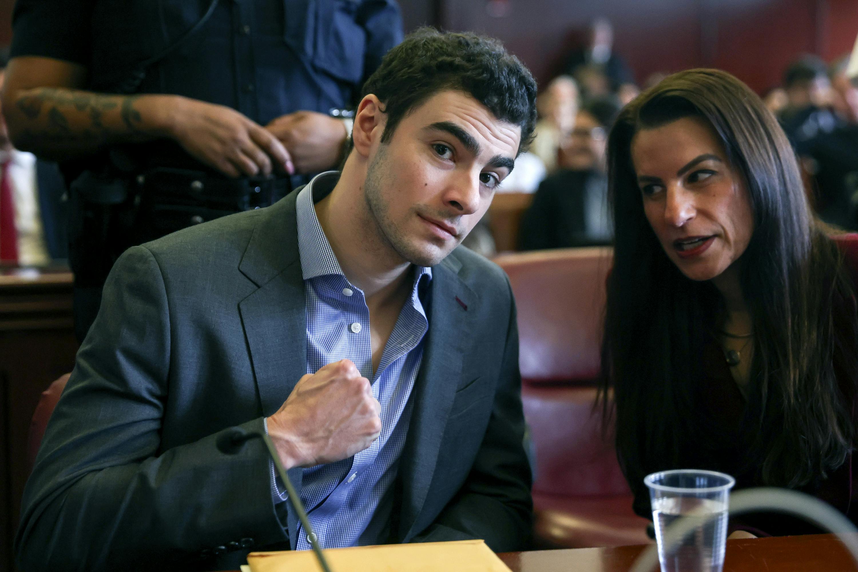 Luigi Mangione flexes for the camera as his lawyer speaks to him.