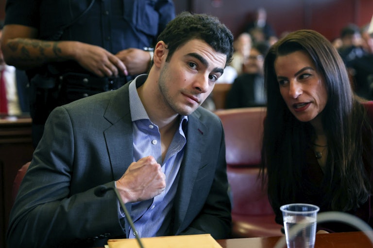 Luigi Mangione flexes for the camera as his lawyer speaks to him.