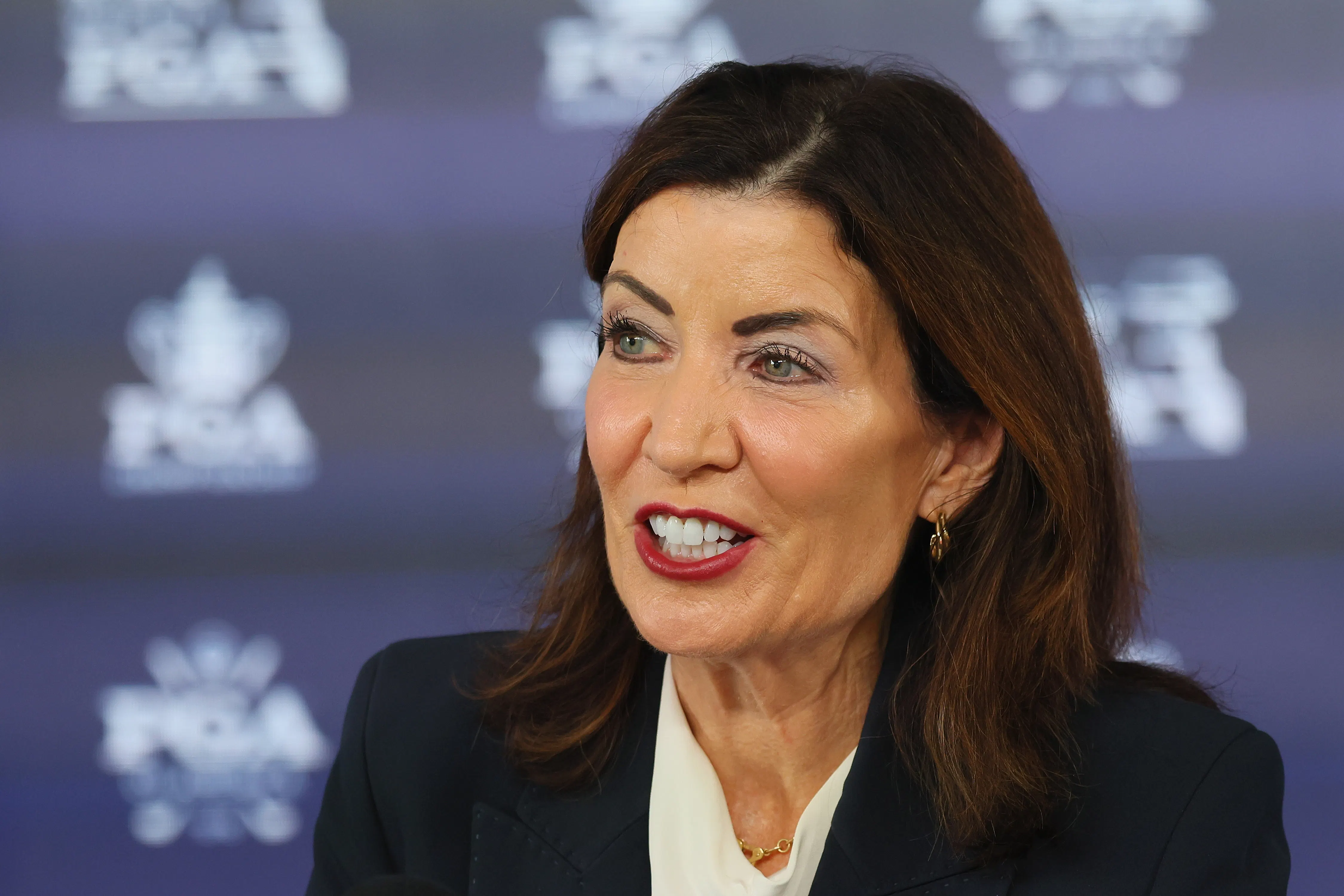Kathy Hochul speaks in front of a blue background with a pattern.