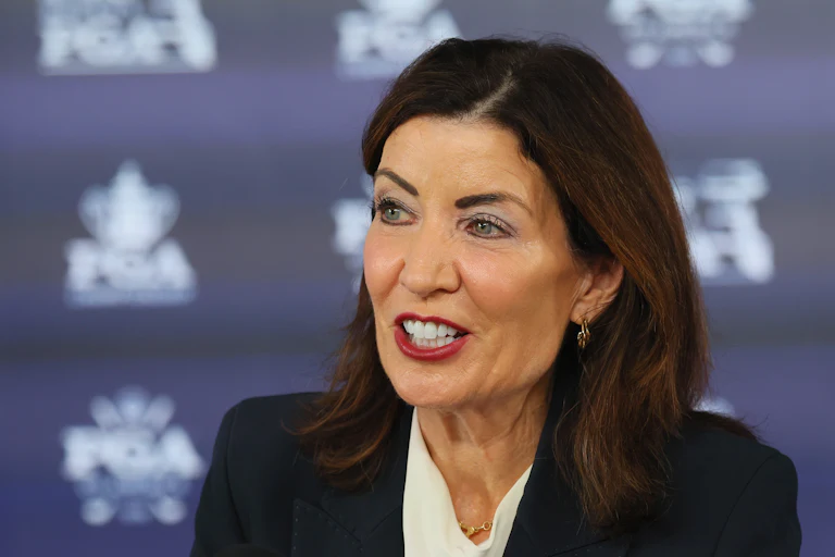 Kathy Hochul speaks in front of a blue background with a pattern.